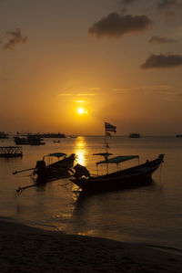 Silhouette boats moored in sea against orange sky