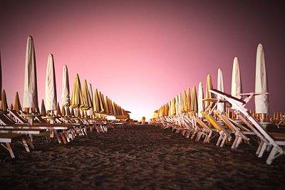 Closed parasol by lounge chairs at beach against clear sky