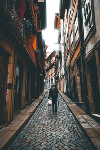 Rear view of man walking on street amidst buildings