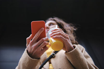 Woman looking away holding smoothie cup and smart phone