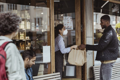 Male customer collecting order from female owner at deli store during pandemic