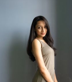 Portrait of a smiling young woman standing against wall