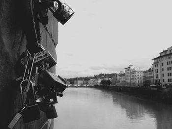 Close-up of padlocks hanging on rope at wall by river against sky