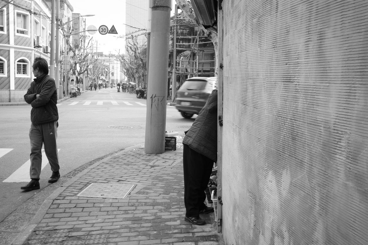 REAR VIEW OF MAN WALKING ON FOOTPATH BY STREET