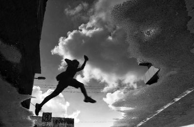 Low angle view of silhouette person jumping in city against sky