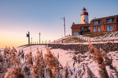 Snow covered field by building against sky during sunset