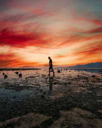 Silhouette woman walking at beach against sky during sunset