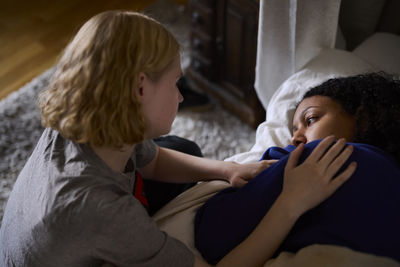 Young woman comforting friend lying in bed