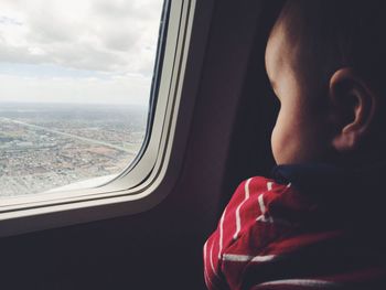 Close-up of boy looking through airplane window