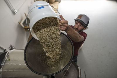 High angle view of man putting raw beans in coffee roaster at shop