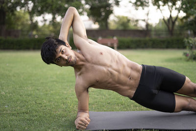 Full length of shirtless young man sitting on grass