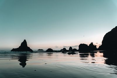 Silhouette rocks in sea against clear sky during sunset
