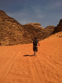 Rear view of man walking on mountain against sky