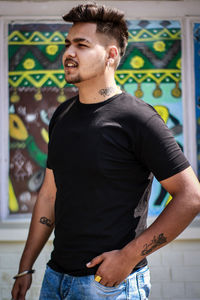 Young man looking away while standing against wall