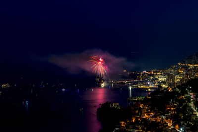 Firework display over illuminated city against sky at night