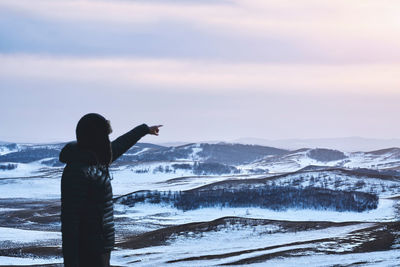 Side view of mature man standing on snowcapped mountain against cloudy sky during sunset