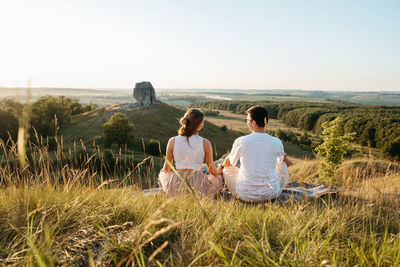 Man and woman practicing yoga and meditation outdoors at sunset with scenic landscape