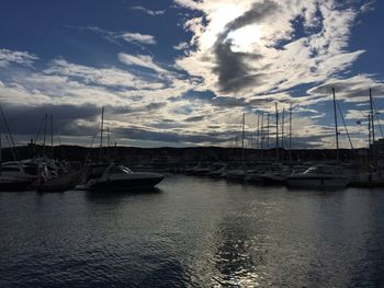 Sailboats moored at harbor against cloudy sky