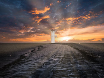 Rear view of woman walking at beach against sky during sunset