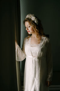 Portrait of young woman standing against curtain