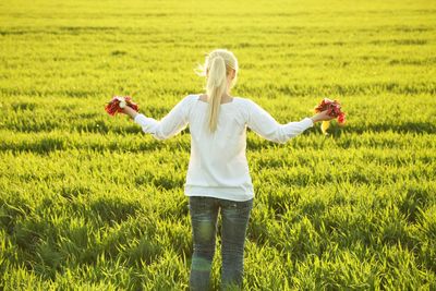 Rear view of woman standing in field with flowers