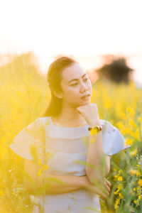Thoughtful woman standing amidst oilseed rape flowers