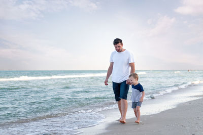 Full length of father and daughter on beach against sky