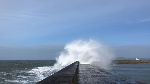 Sea waves splashing on pier against sky