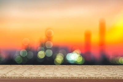 Defocused image of illuminated lights against sky during sunset