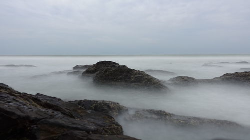 Rock formations by sea against sky in foggy weather