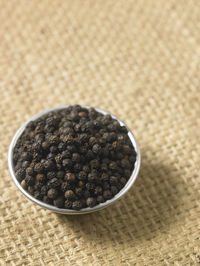 Close-up of black peppercorns in bowl on burlap
