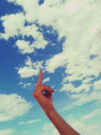 Low angle view of cropped hand against cloudy sky