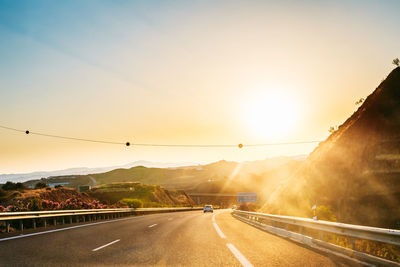 Road by mountains against sky during sunset