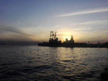 Silhouette cranes in sea against sky during sunset