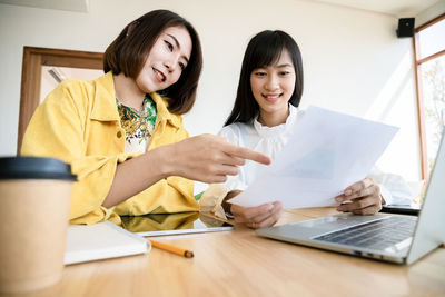 Portrait of a smiling young woman using phone while sitting on table