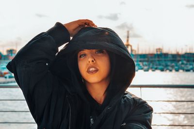 Portrait of beautiful young woman in hooded jacket standing against sky