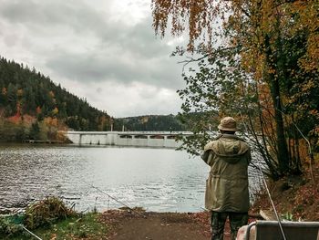 Rear view of man standing by lake against sky