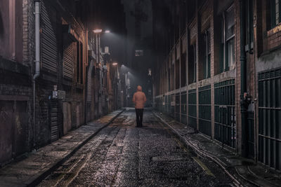 Rear view of man walking on alley amidst buildings in city