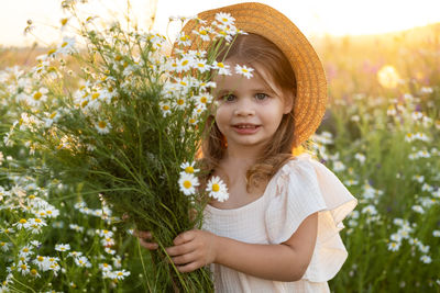 Portrait of cute girl wearing hat standing in flowering field