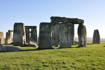 Historic stonehenge on grassy field against clear sky