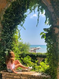 Woman sitting by tree against sea