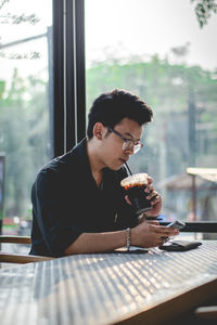 Young man using mobile phone while drinking coffee at restaurant