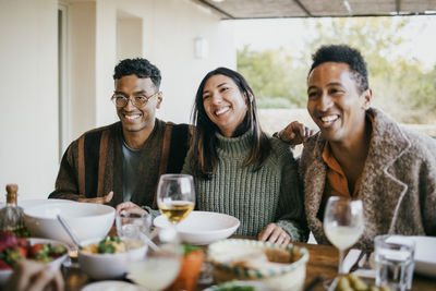 Cheerful woman sitting with male friends at dining table in patio enjoying dinner party