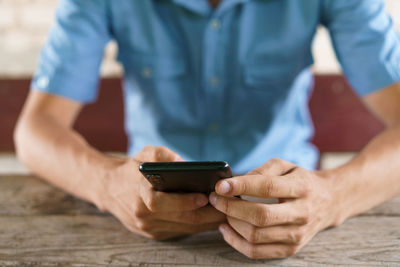 Young man sits on street at table with phone in his hand.