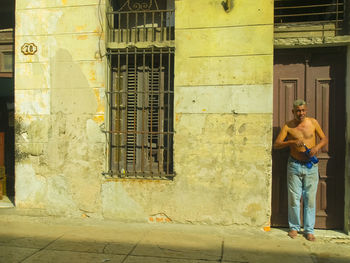 Rear view of shirtless man standing on sidewalk against building