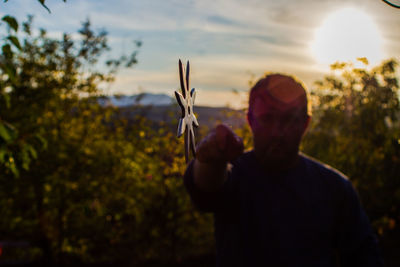 Man throwing shuriken while standing on field against sky during sunset