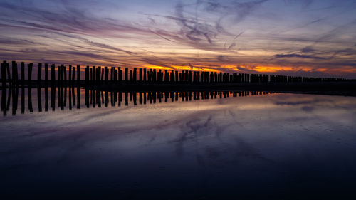 Silhouette pier with reflection on sea against cloudy sky at sunset
