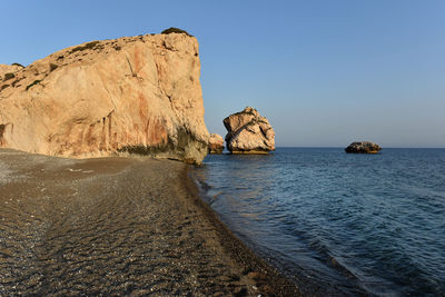 Rock formation by sea against clear sky