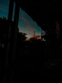 Silhouette trees by buildings against sky at sunset