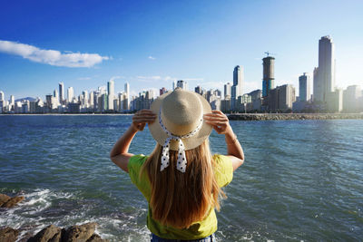 Young woman with hat looking to skyline full of skyscrapers on south coast of brazil.